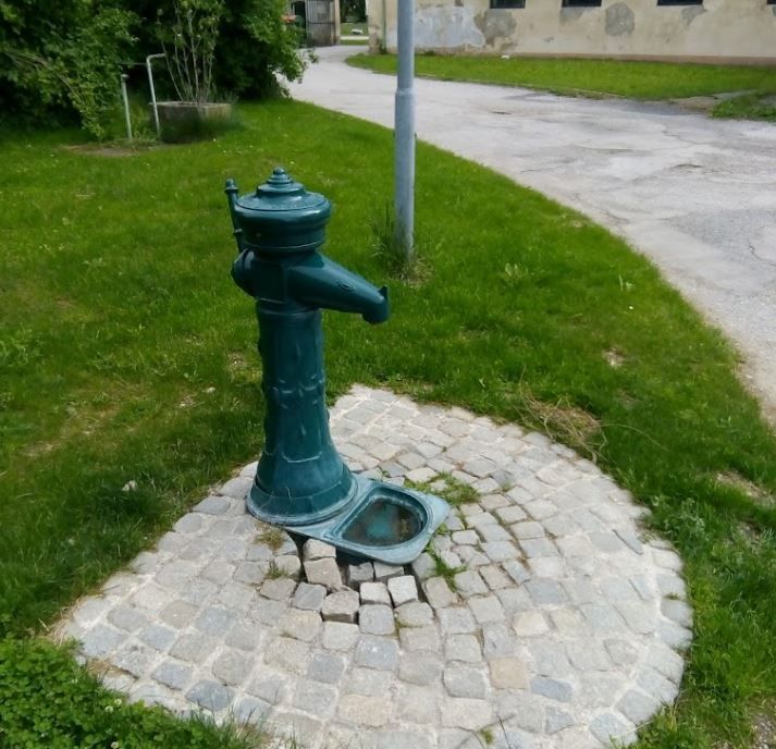 Ein grüner Trinkwasserbrunnen auf einem gepflasterten Platz im Freien.