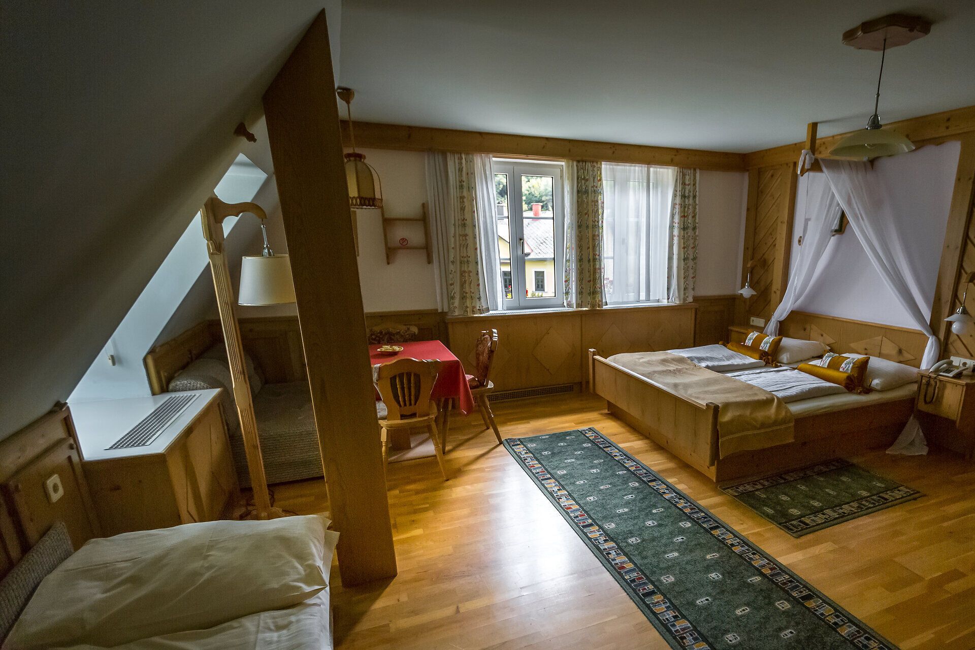 In den Zimmern im Hotel Raxalpenhof steht ein Holzbett mit Baldachin.