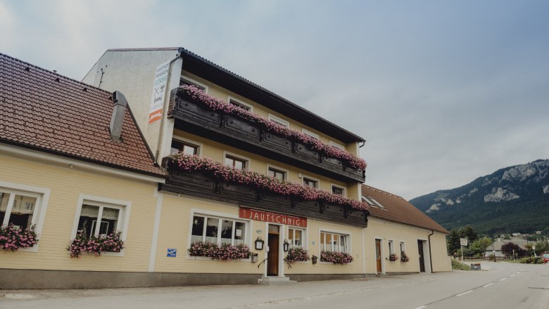 Ein traditioneller Landgasthof mit Blumen geschm&uuml;ckten Balkonen vor einer Bergkulisse.