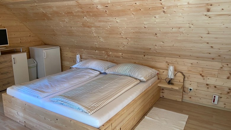 Ein gemütliches Doppelzimmer mit Holzverkleidung, einem Doppelbett, einem kleinen Kühlschrank und einem Fernseher auf einer Kommode.