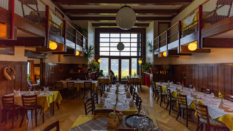 Innenansicht eines Restaurants mit Holzmöbeln und großen Fenstern.