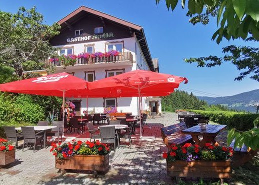 A traditional inn with a terrace, red parasols and flower boxes against a clear blue sky.