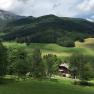 A farm in a green, hilly landscape with mountains in the background.