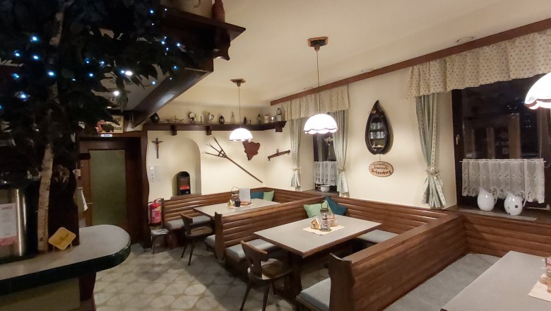 Gemütliche Gaststube mit Holzmöbeln, dekorativen Vorhängen und rustikalen Accessoires.