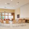 An empty seminar room with a circle of chairs, projector, screen and flipchart.