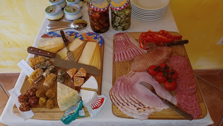 Fr&uuml;hst&uuml;cksbuffet mit K&auml;se, Aufschnitt, Tomaten und Paprika auf Holzbrettern.