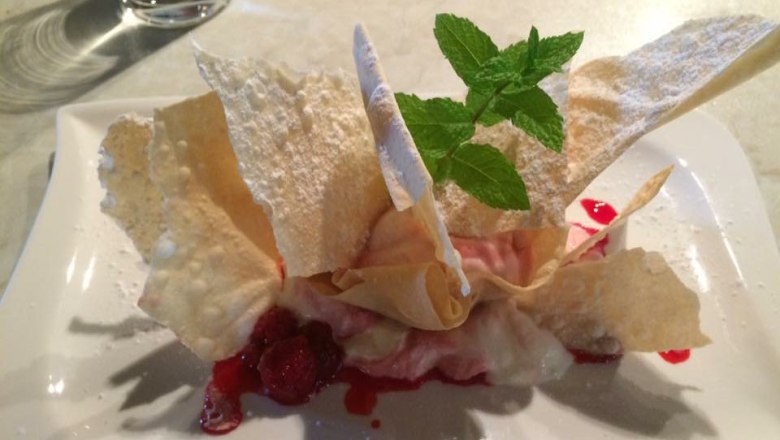 A dessert with raspberries, thin pastry sheets and mint on a white plate.