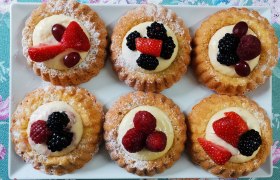 Sechs kleine Obsttörtchen auf einem weißen Teller, dekoriert mit Beeren und Sahne.