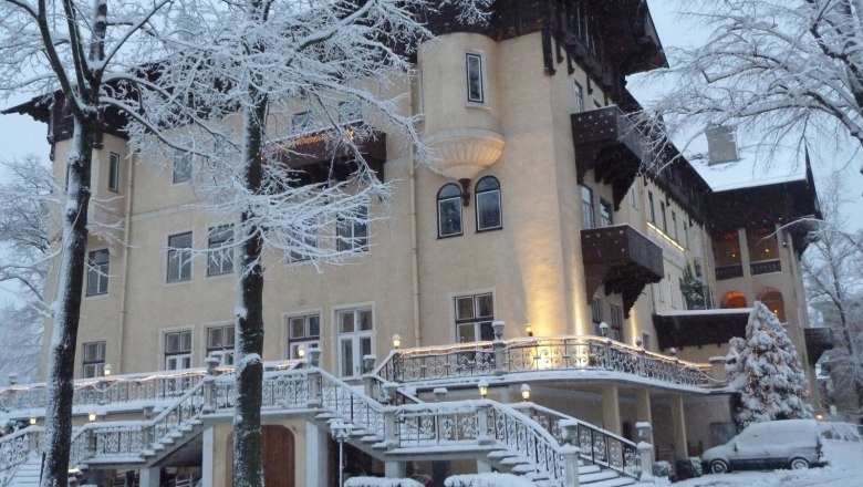 Ein großes, elegantes Hotel im Winter, umgeben von schneebedeckten Bäumen und einem verschneiten Auto.