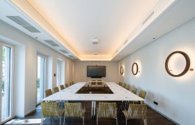 Moderner Seminarraum mit U-förmiger Tischanordnung, Stühlen, einem großen Bildschirm und dekorativen Wandlampen.