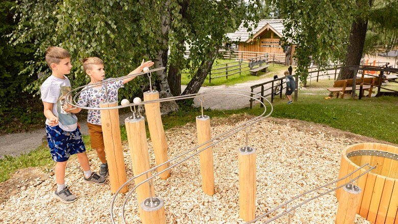 Zwei Kinder spielen an einer Kugelbahn im Freien.