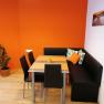 A modern breakfast room with an orange wall, black corner bench, table and chairs. A plant stands in the corner, a picture hangs on the wall.