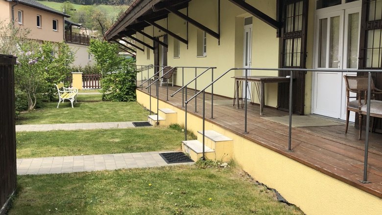 Außenansicht eines gelben Gebäudes mit Veranda und Berg im Hintergrund.