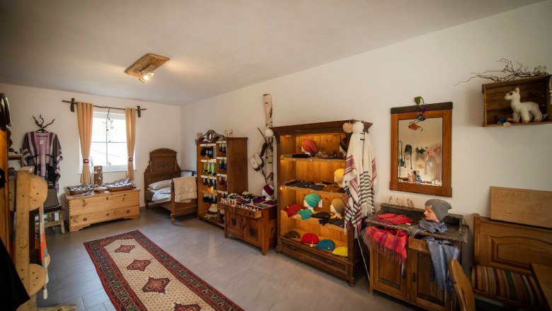 Innenansicht eines Hofladens mit Alpakaprodukten, Holzmöbeln und Teppich.