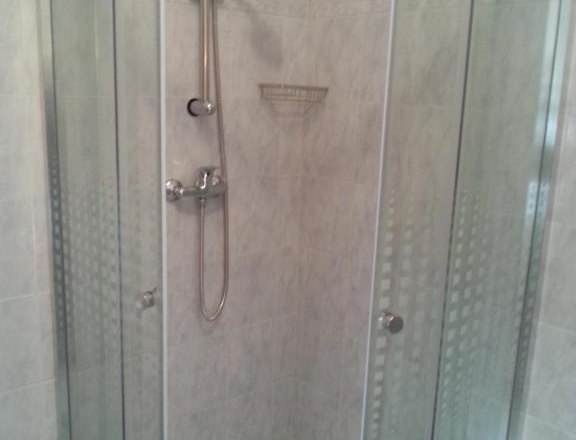 Eckdusche mit Glastüren und Duschkopf in einem gefliesten Badezimmer.