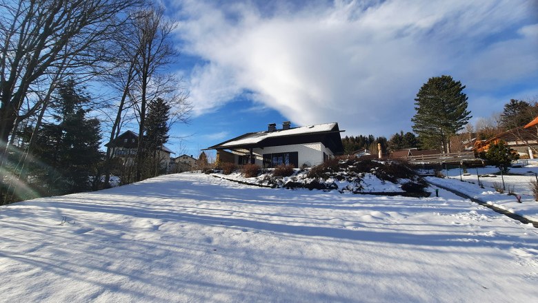 Winter landscape with a house in the snow, surrounded by trees and blue sky.