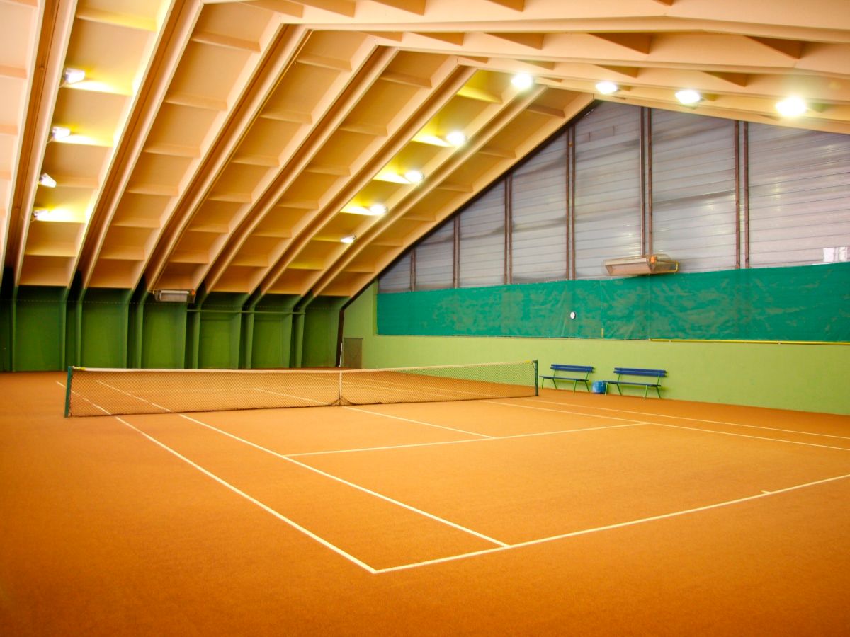 An interior view of an indoor tennis facility with a tennis court and green walls.