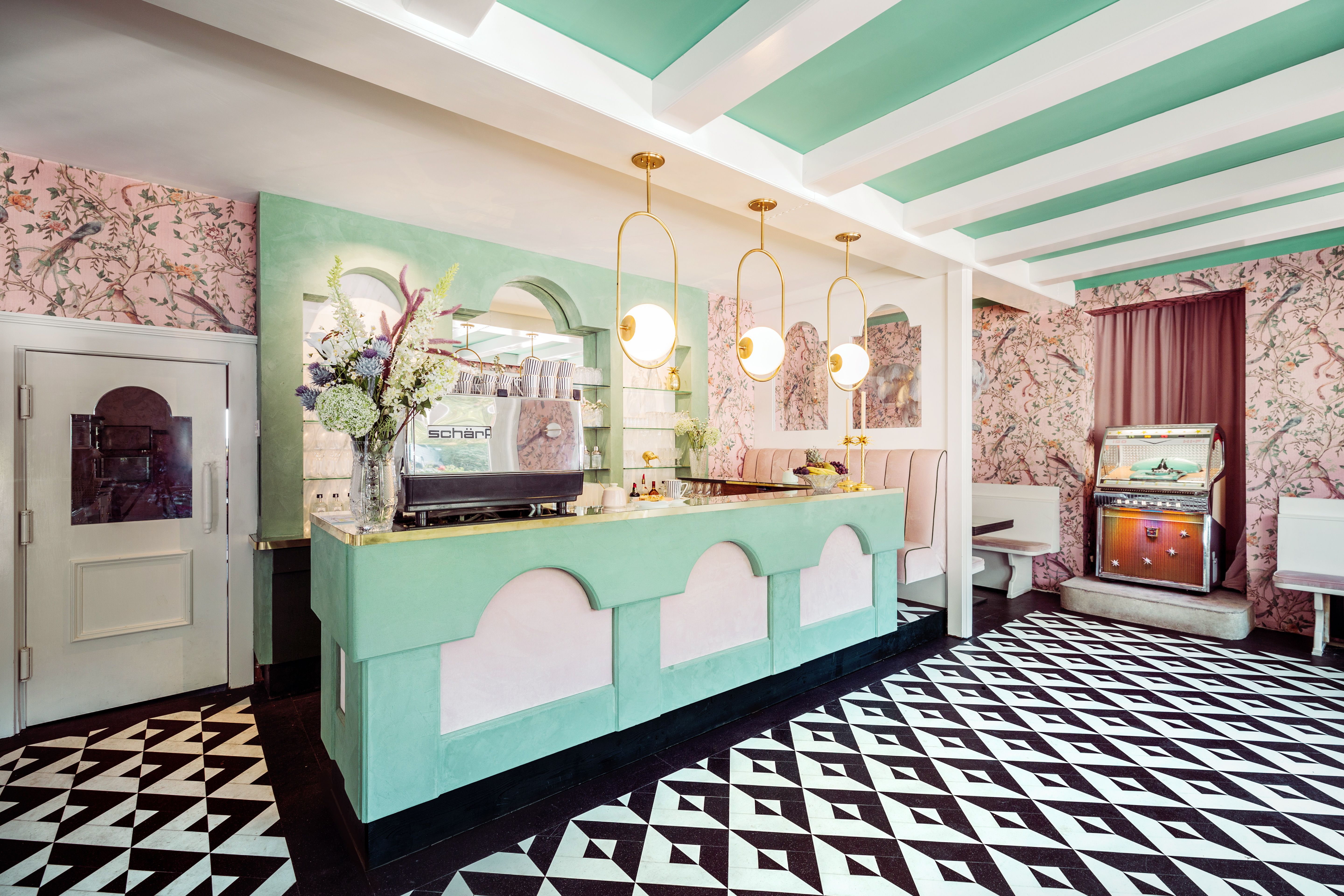 Innenansicht eines stilvollen Cafés mit pastellfarbenem Dekor, geometrischem Bodenmuster und einer Jukebox.