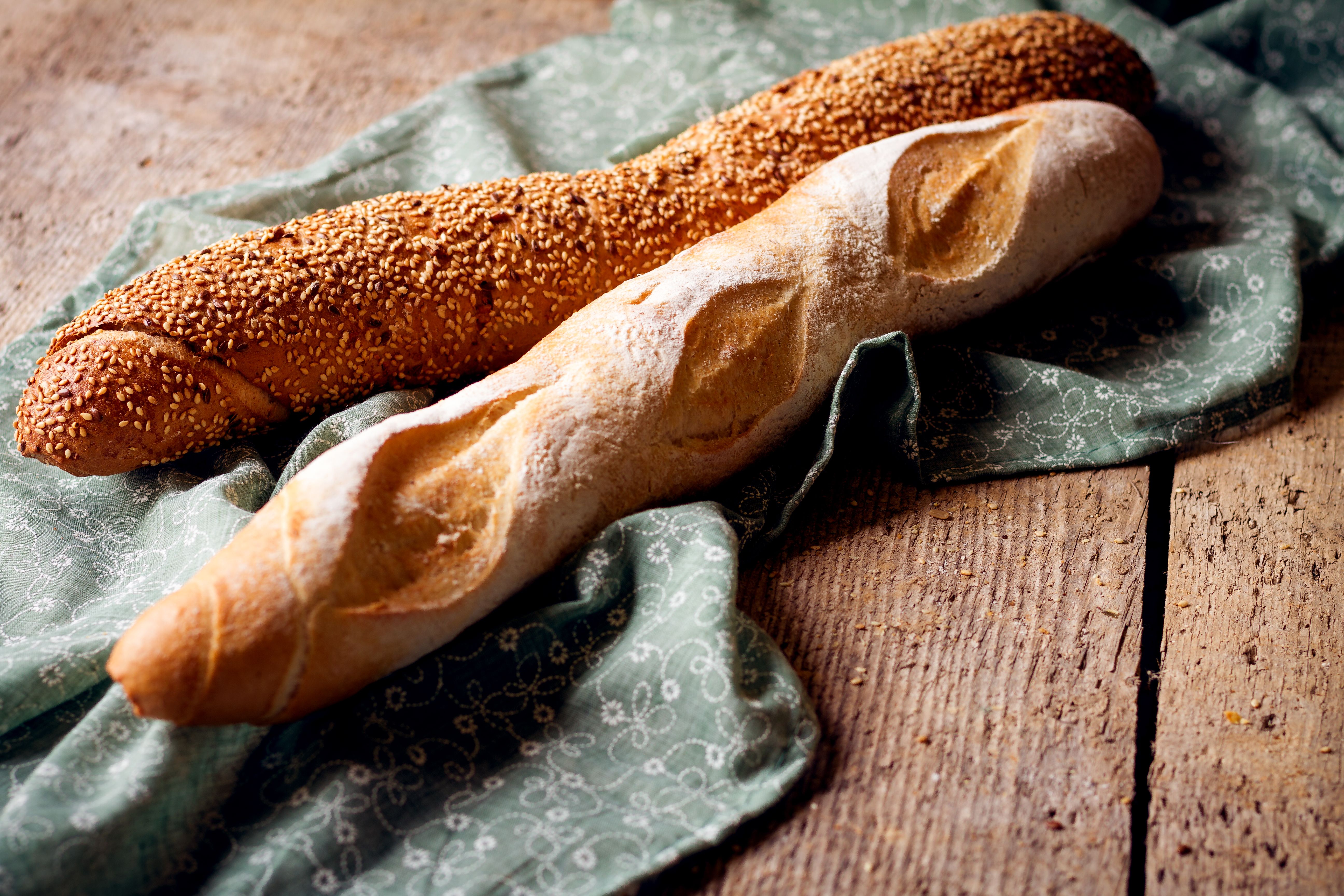 Ein Baguette mit Körnern und ein weißes Baguette auf einem grünen Tuch.