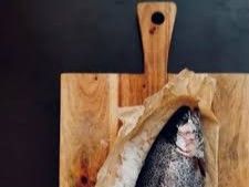 Ein Fisch in Papier eingewickelt auf einem Holzbrett.