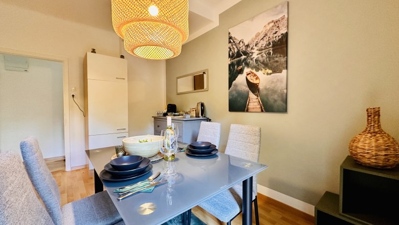 Esszimmer mit Glastisch, grauen Stühlen und großem Lampenschirm.