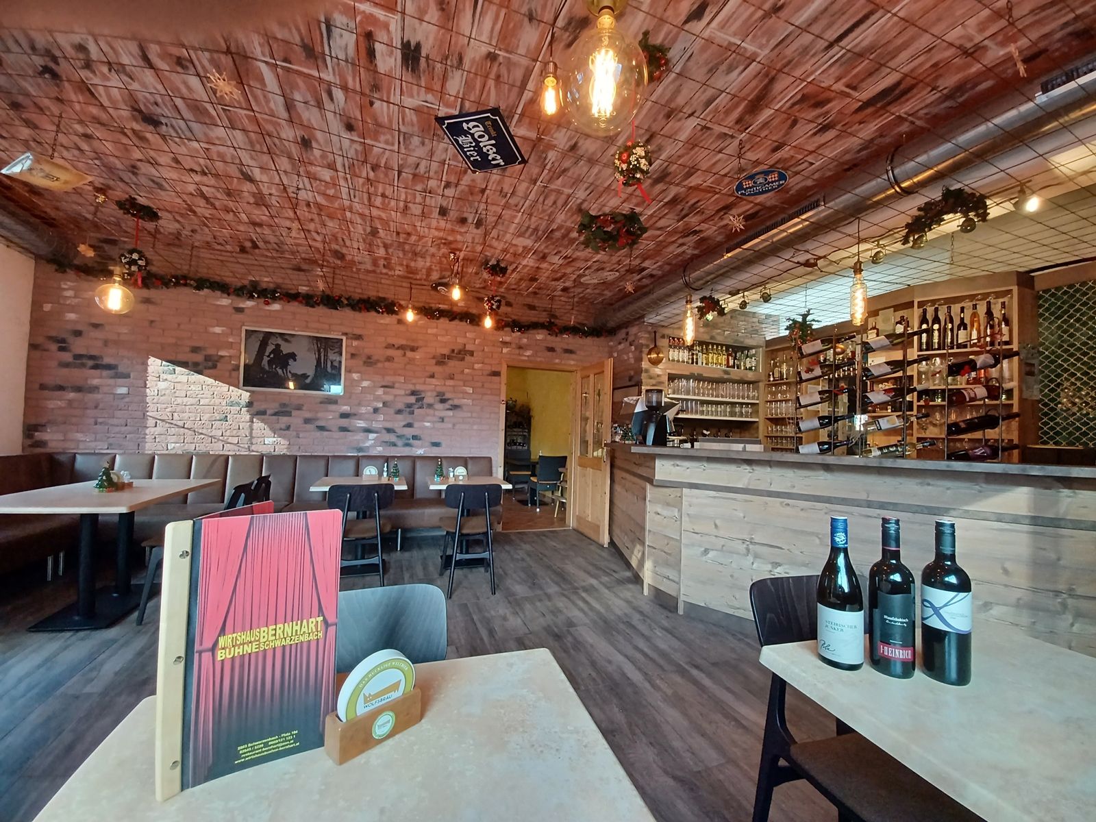 Gemütliche Gaststube mit Holztischen, Bar und Weinflaschen.