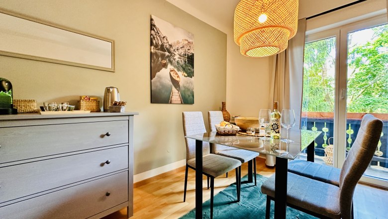 Gemütliches Esszimmer mit Tisch, Stühlen und Hängelampe, Blick auf Balkon und Natur.