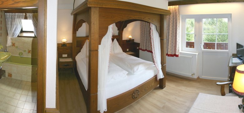 Gemütliches Schlafzimmer mit Himmelbett, angrenzendem Badezimmer und Balkonzugang.