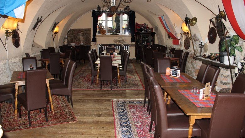 A vaulted hall with tables and chairs, decorated with carpets and flags.