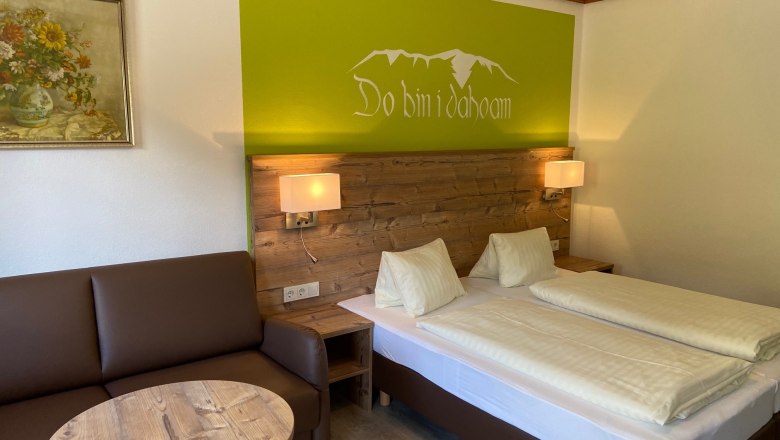 Gemütliches Doppelzimmer mit Holzmöbeln, Sofa, Tisch und Wanddekoration.