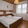 A traditionally furnished double room with wooden furniture, a double bed, a cross on the wall and a window with curtains.
