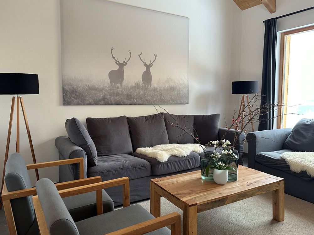 Wohnzimmer mit grauen Sofas, Holztisch und Hirschbild an der Wand.