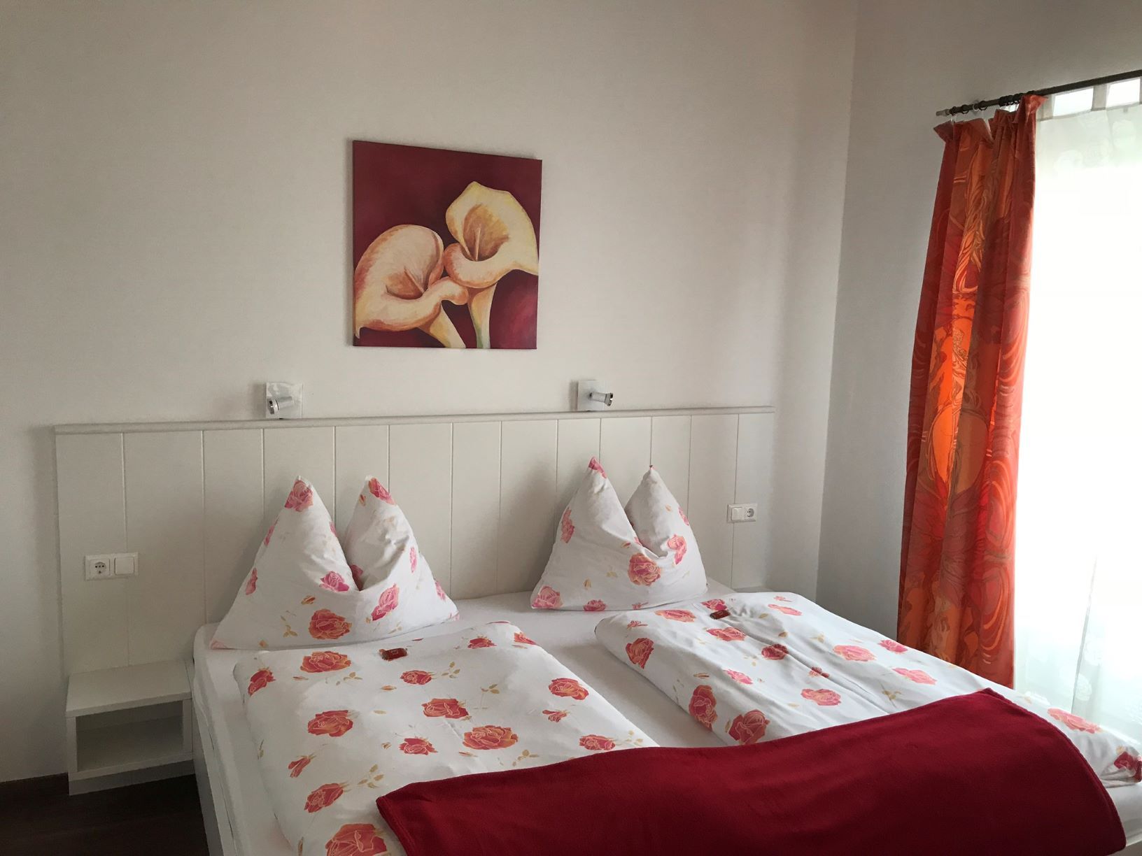 Schlafzimmer mit Doppelbett, Blumenbettwäsche, rotem Bild und Vorhängen.