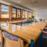 A bright seminar room with large windows, U-shaped tables, chairs and a flipchart.