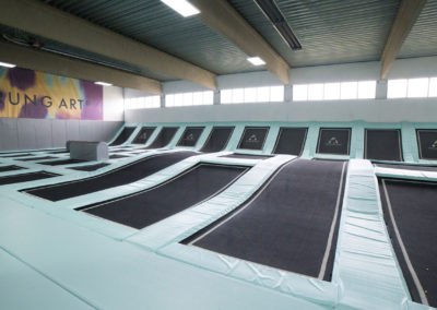 Innenansicht eines Trampolinparks mit mehreren Trampolinen in einer Halle.