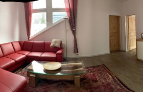 Wohnzimmer mit rotem Ledersofa, Glastisch, Teppich und TV auf Holzschrank.