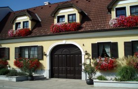 Yellow house with red flowers and brown roof.