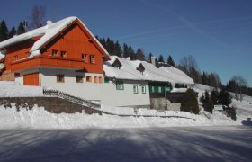 Verschneites Gasthaus mit Holzfassade und blauen Himmel im Hintergrund.