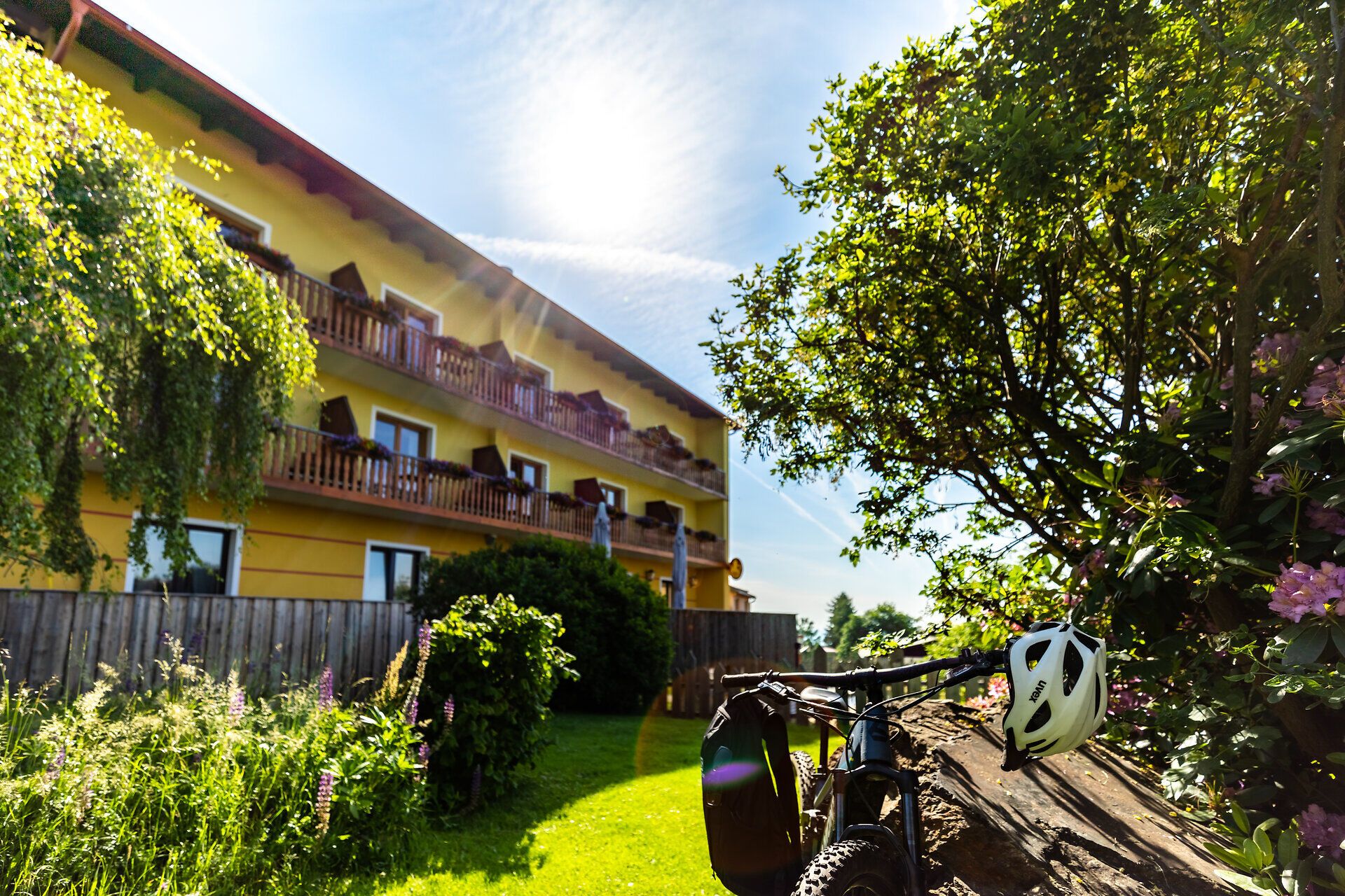 Ein Fahrrad mit Radhelm an der Lenkstange parkt im Garten vor der Rückseite des Sonnenhof Hechtl. 