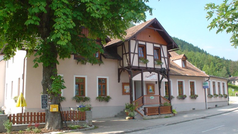 Traditionelles Gasthaus, davor Blumenkästen, umgeben von Bäumen.