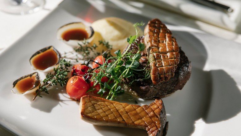 Gourmetgericht mit Steak, Pilz, Tomaten und So&szlig;e auf einem wei&szlig;en Teller.