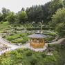 A wooden pavilion in a well-tended garden with green trees and stone paths.