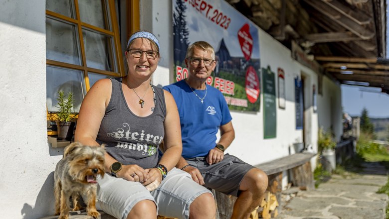 Zwei Personen sitzen vor einem Geb&auml;ude mit einem Hund, im Hintergrund ein Plakat mit Datum 09. Sept. 2023.