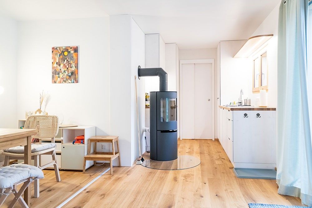 Moderner Wohnbereich mit Holzfußboden, Kaminofen, Esstisch und Küchenzeile.