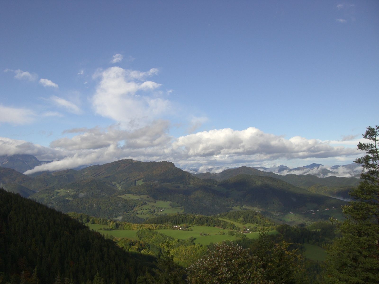 Panoramablick auf eine grüne Berglandschaft unter blauem Himmel mit Wolken.