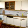 Kitchenette with white cupboards, stove, sink and dishwasher.