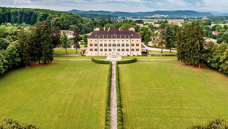 Aerial view of Frohsdorf Castle with its yellow façade, long, straight driveway and well-tended park.