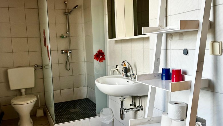 Modernes Badezimmer mit Dusche, Waschbecken, WC und Regal mit Toilettenpapier und Bechern.