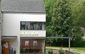 Modern building with the inscription 'Gasthaus Burgkeller', surrounded by trees.