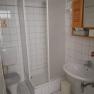 A small, white tiled bathroom with shower, toilet and washbasin.